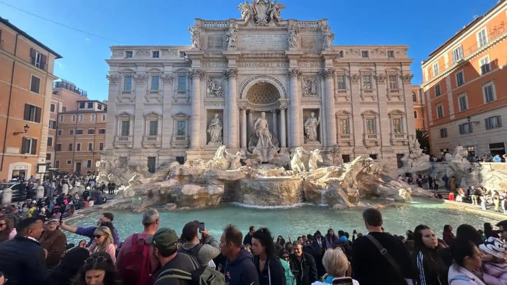 o: Imagem da Fontana di Trevi em Roma cercada por grande quantidade de visitantes, demonstrando a superlotação que motivou a criação da taxa de 2 euros para acesso ao monumento.